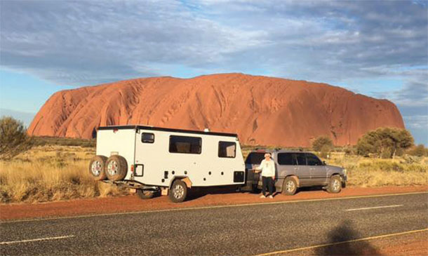 Offroad caravan parked on a, outback road with Uluru in the background