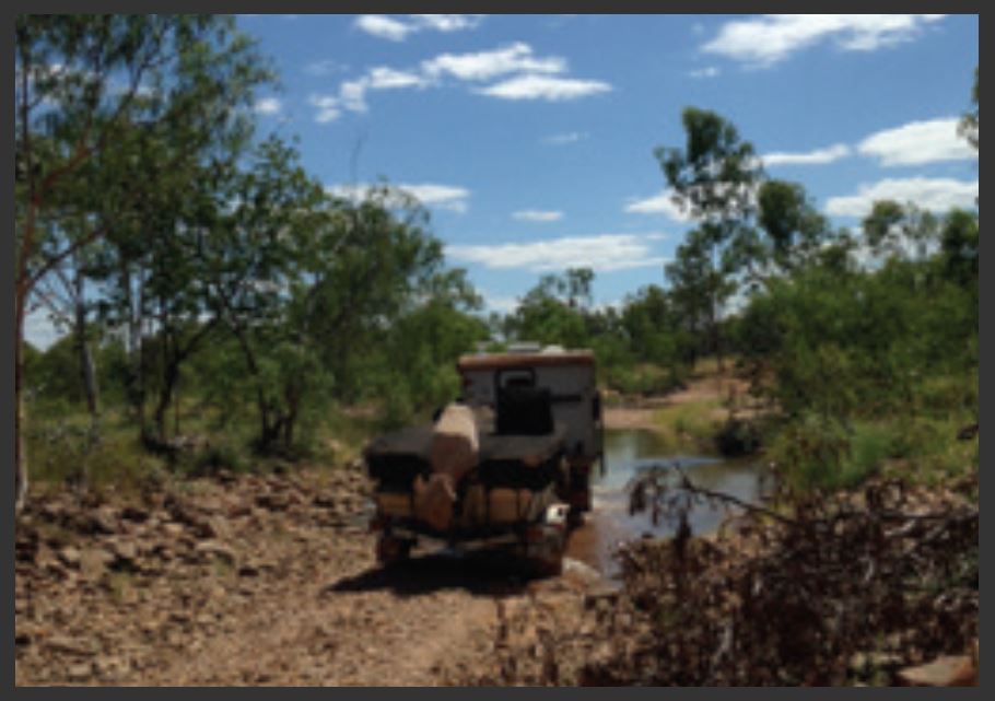 Rear-view of an offroad boat trailer carrying a boat through a rugged river crossing