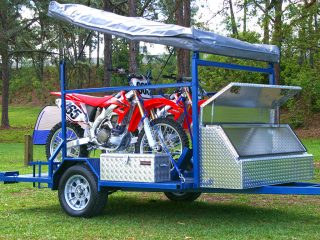 Blue dirt bike camper trailer loaded with two red dirt bikes and an overhead tent