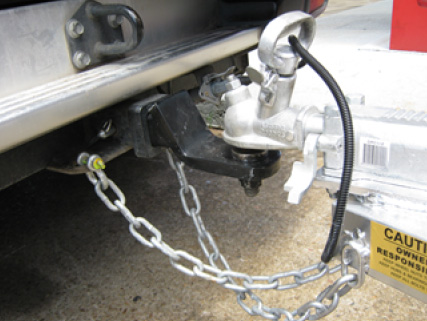 Close up of a trailer coupling connected to a tow bar with safety chains crossed over
